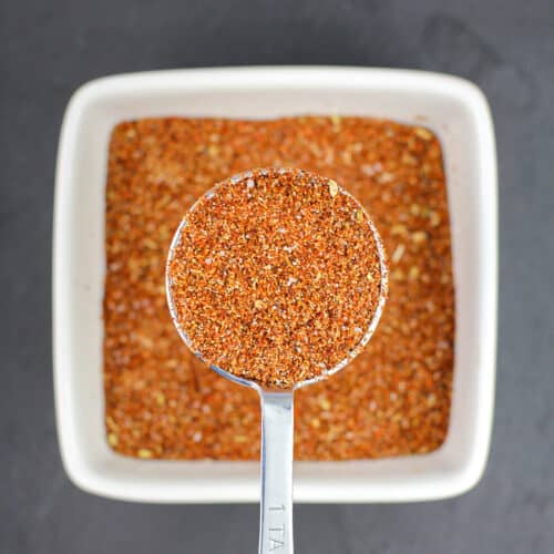 measuring spoon holding homemade taco seasoning over white bowl filled with more seasoning