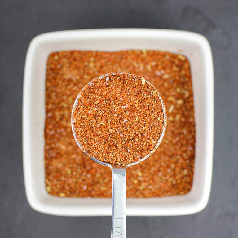 measuring spoon holding homemade taco seasoning over white bowl filled with more seasoning