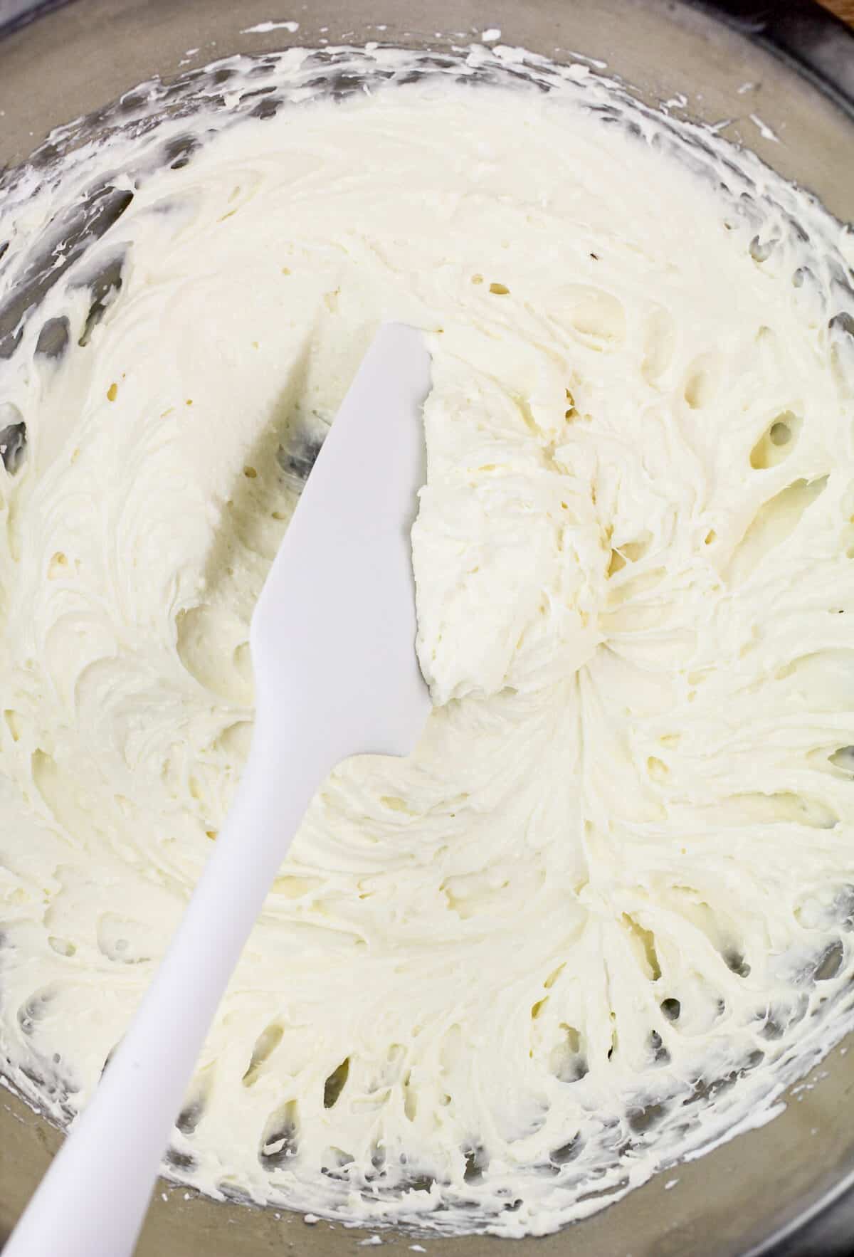 white spatula in glass bowl with cream cheese layer mixture