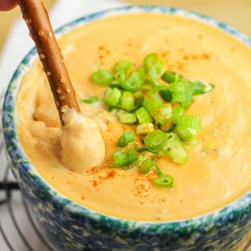 prepared old english cheese spread in blue crock topped with green onion with a pretzel inserted