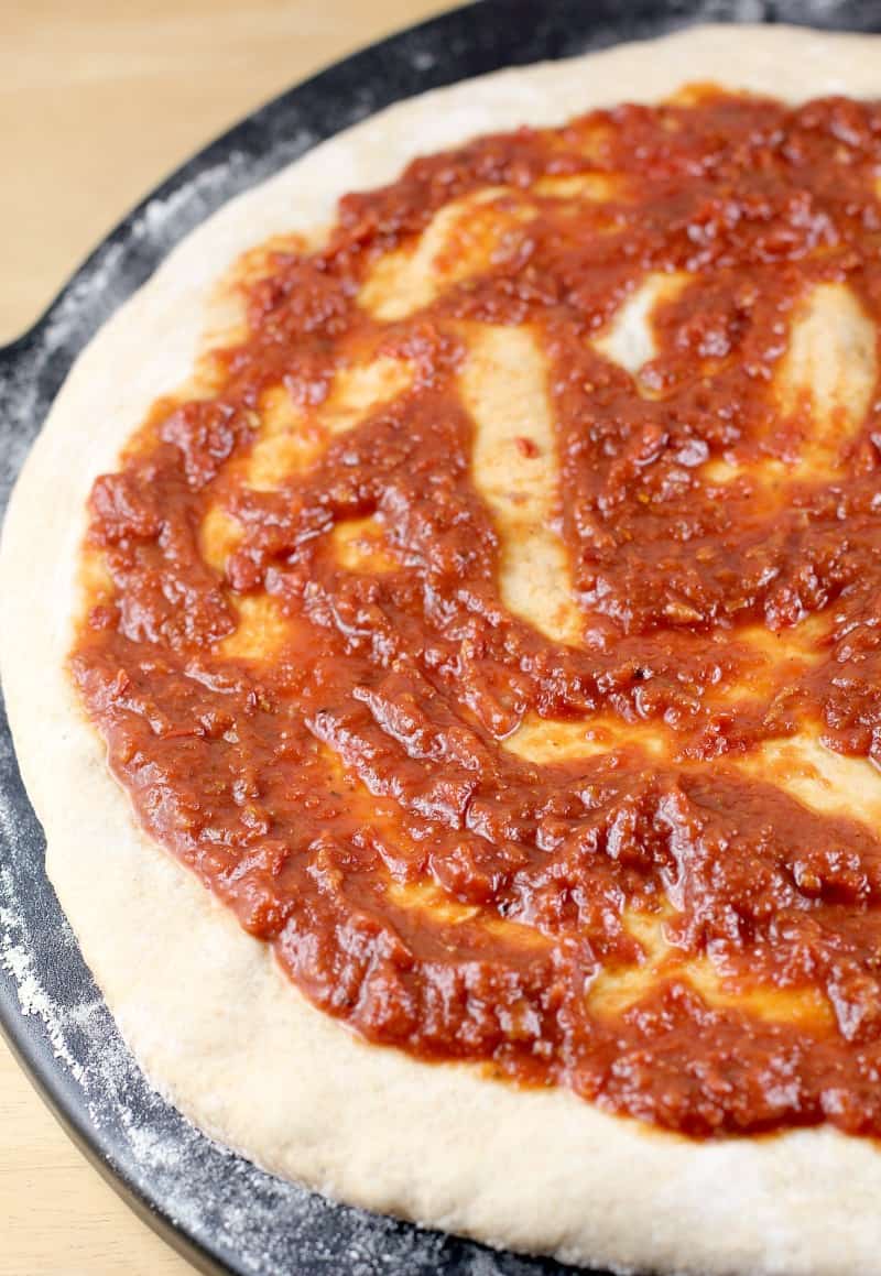 uncooked dough rolled out with a layer of sauce on top