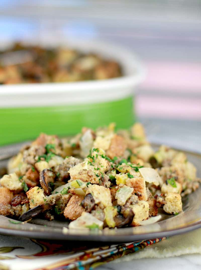 serving of stuffing plated on a brown ceramic plate; casserole in the background