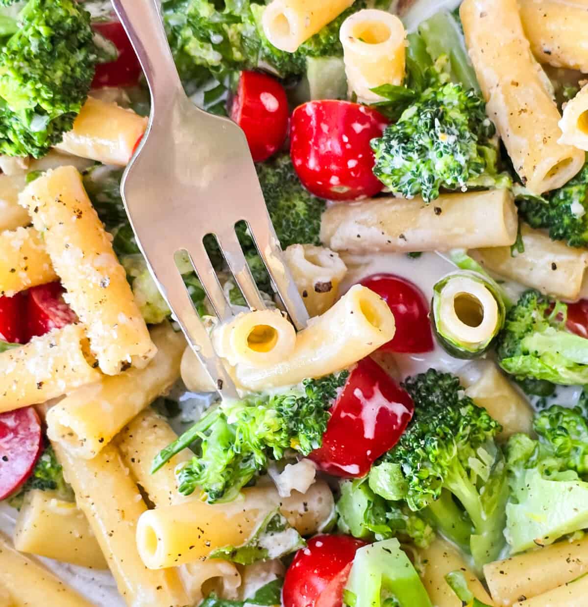 fork inserted into prepared arugula and broccoli pasta