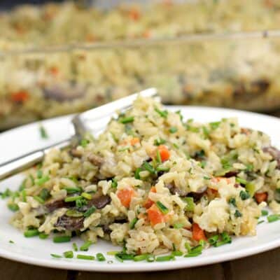 brown rice casserole on a white plate with fork; bake dish in the back ground
