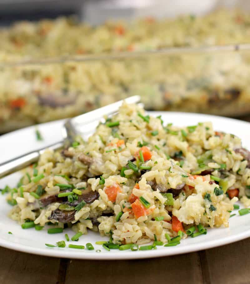 brown rice casserole on a white plate with fork; bake dish in the back ground