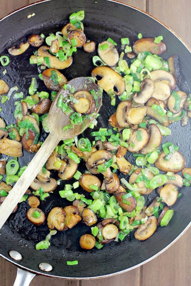browned mushrooms and green onion with wooden spoon in black skillet