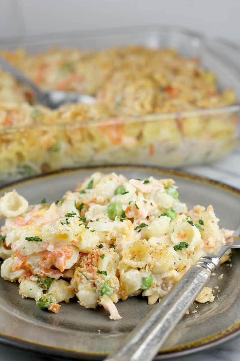 cooked salmon casserole on a serving plate in the foreground, rest of casserole in a bake dish in the background