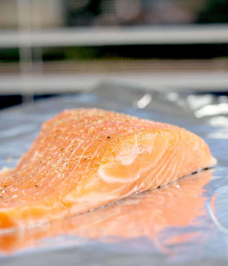 raw salmon on a bake sheet topped with salt and pepper