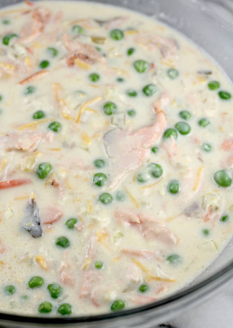 milk, soup, peas, cheese, salmon, and onion combined in a glass mixing bowl