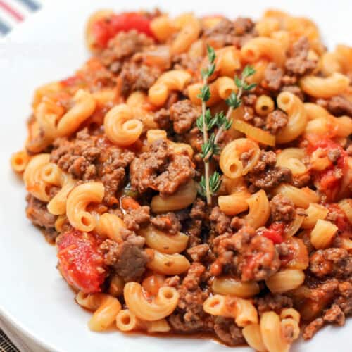 prepared goulash on white dish topped with small sprig of thyme