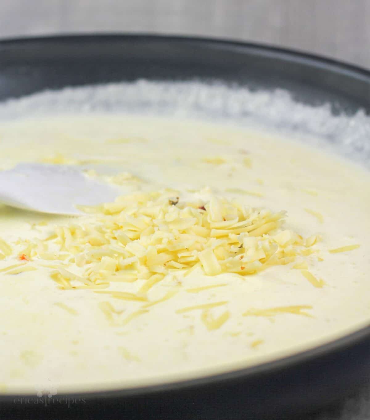 cheese added to alfredo sauce in skillet