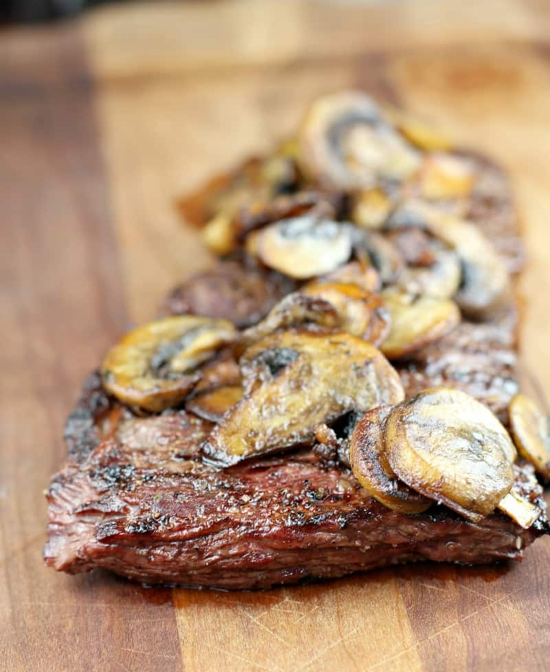 garlic butter skirt steak topped with mushrooms on a wood board