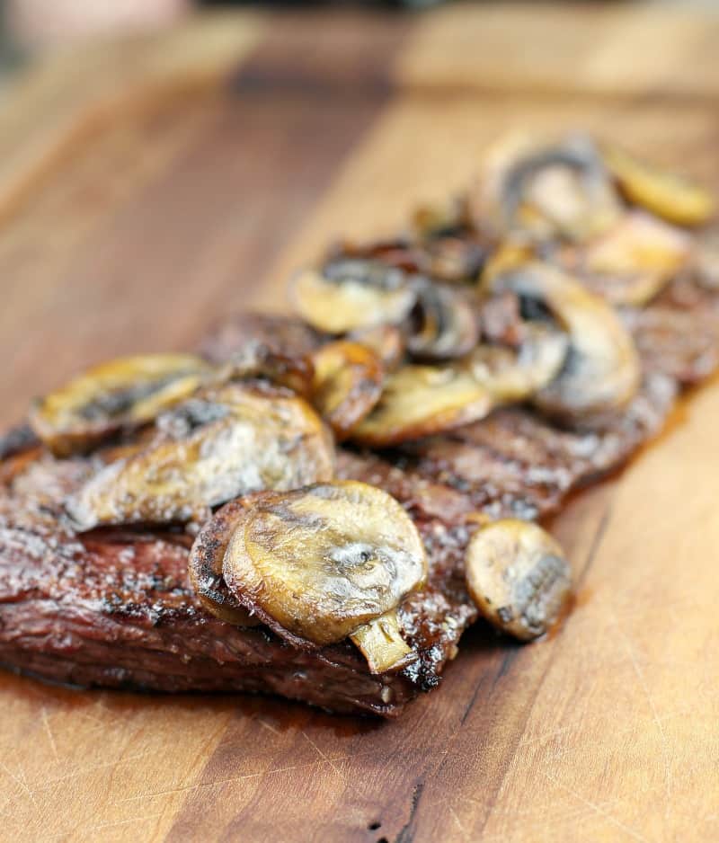side view of steak on board topped with mushrooms