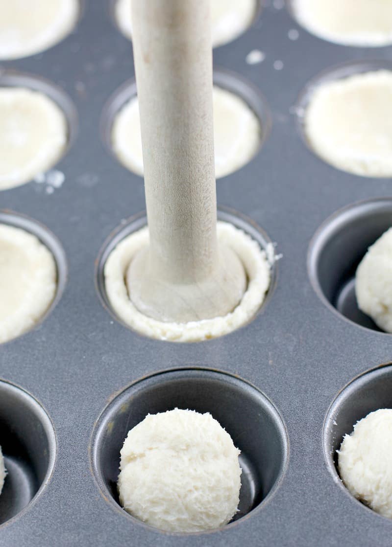 Wood tamper pressing down the cream cheese cookie dough into the mini muffin tin