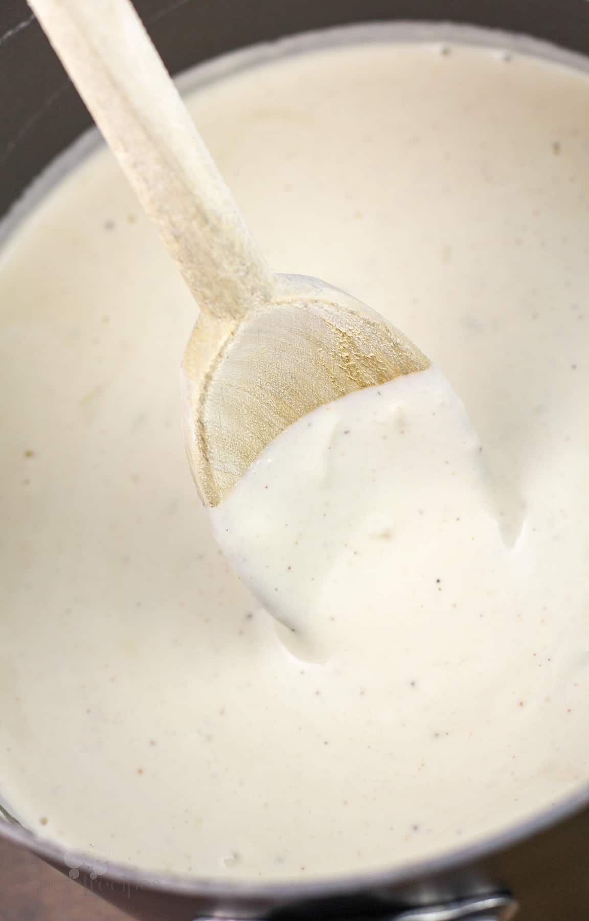 white sauce in pan with wood spoon to show thickness