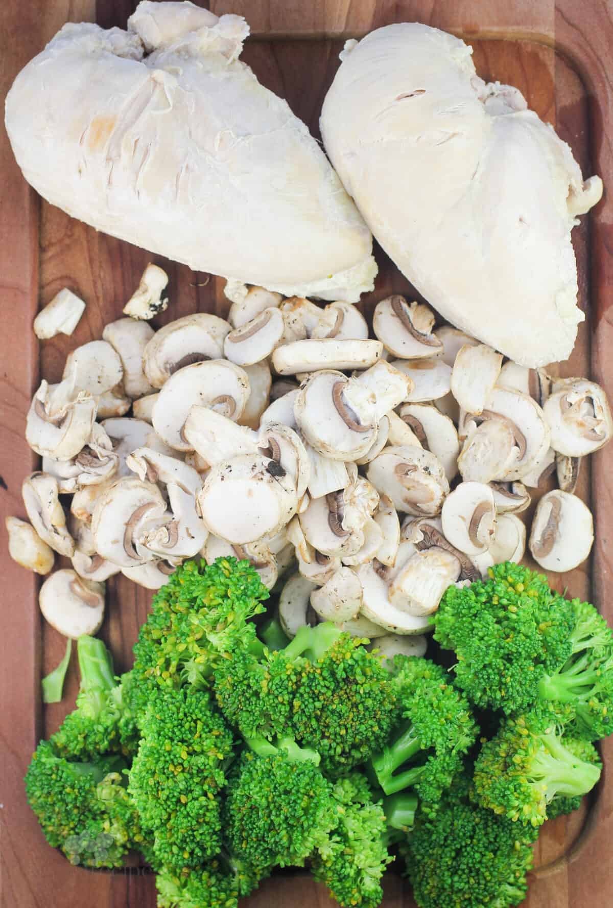 wood board with chicken breasts, mushrooms, and broccoli