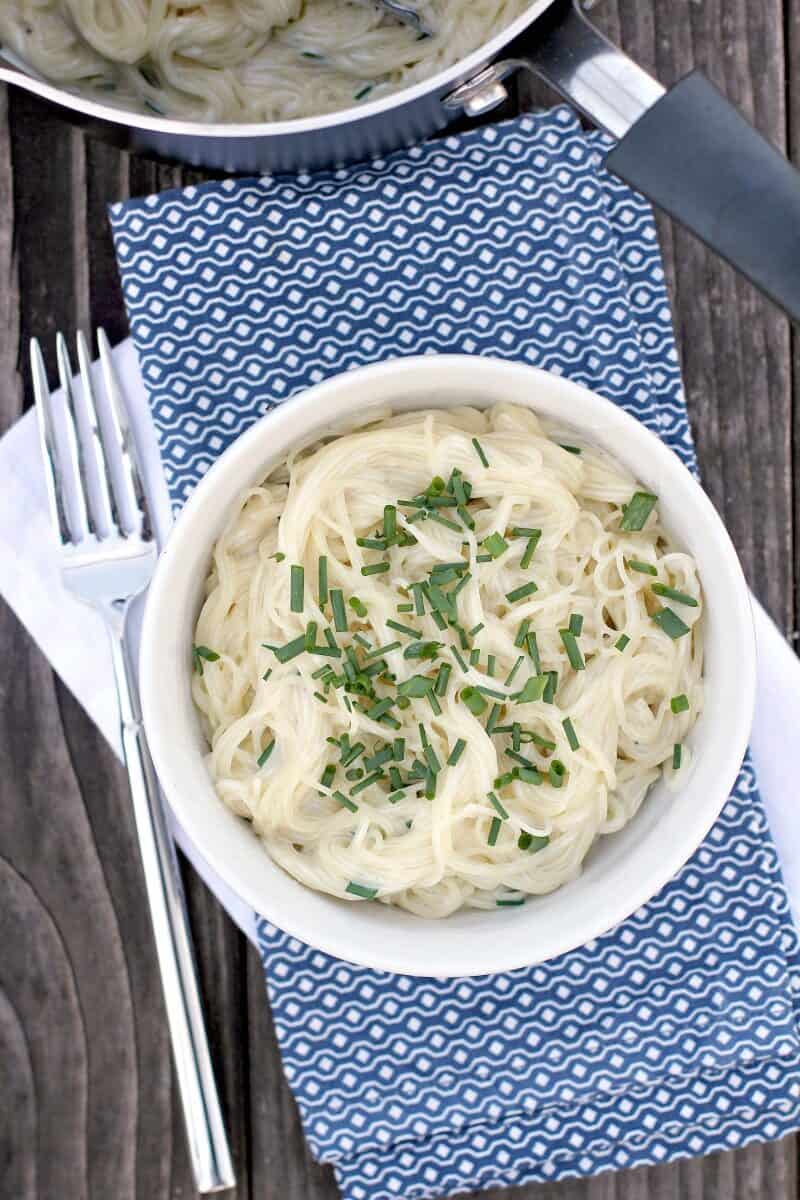 top down view of pasta topped with chives in white bowl on blue napkin