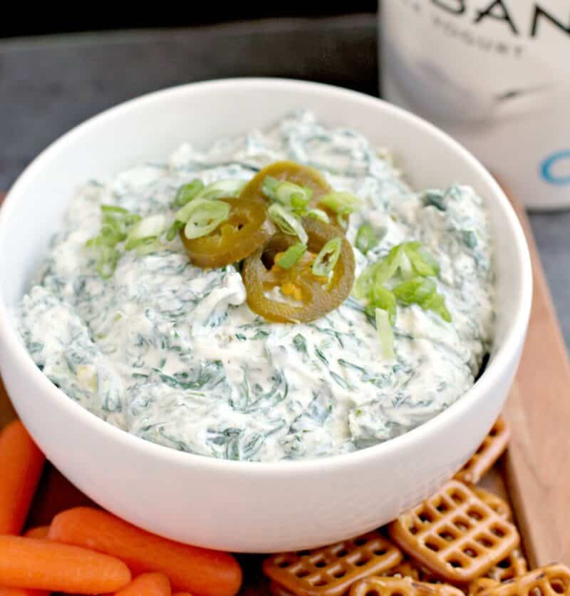 dip in a white bowl on a wood platter with baby carrots and square pretzels