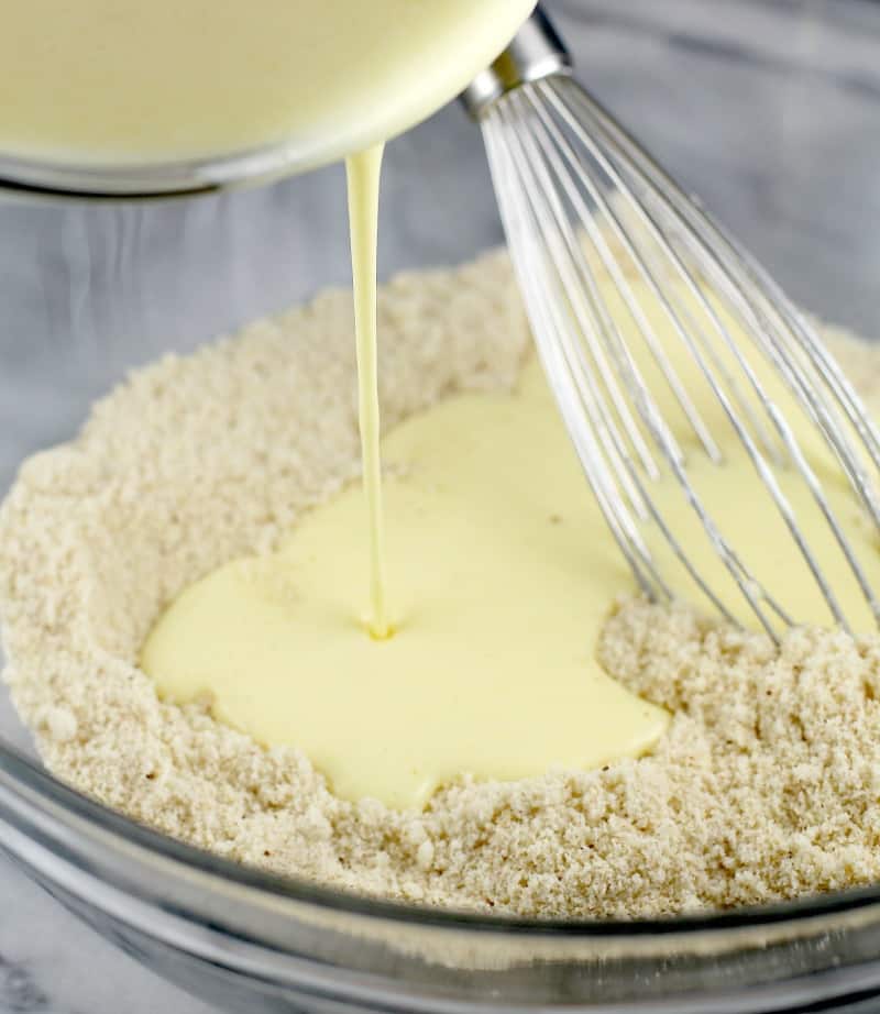 view of wet ingredients being poured into the dry ingredients in a glass bowl