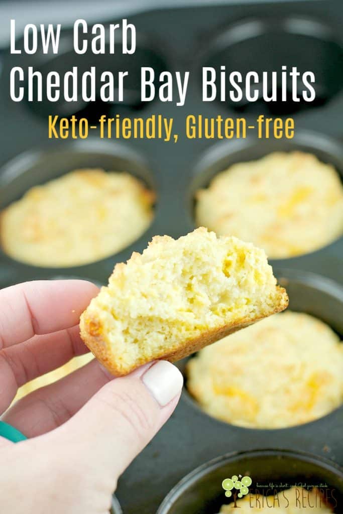 hand holding biscuit broken in half to show flaky inside, other biscuits in muffin tin in the background, pinnable image