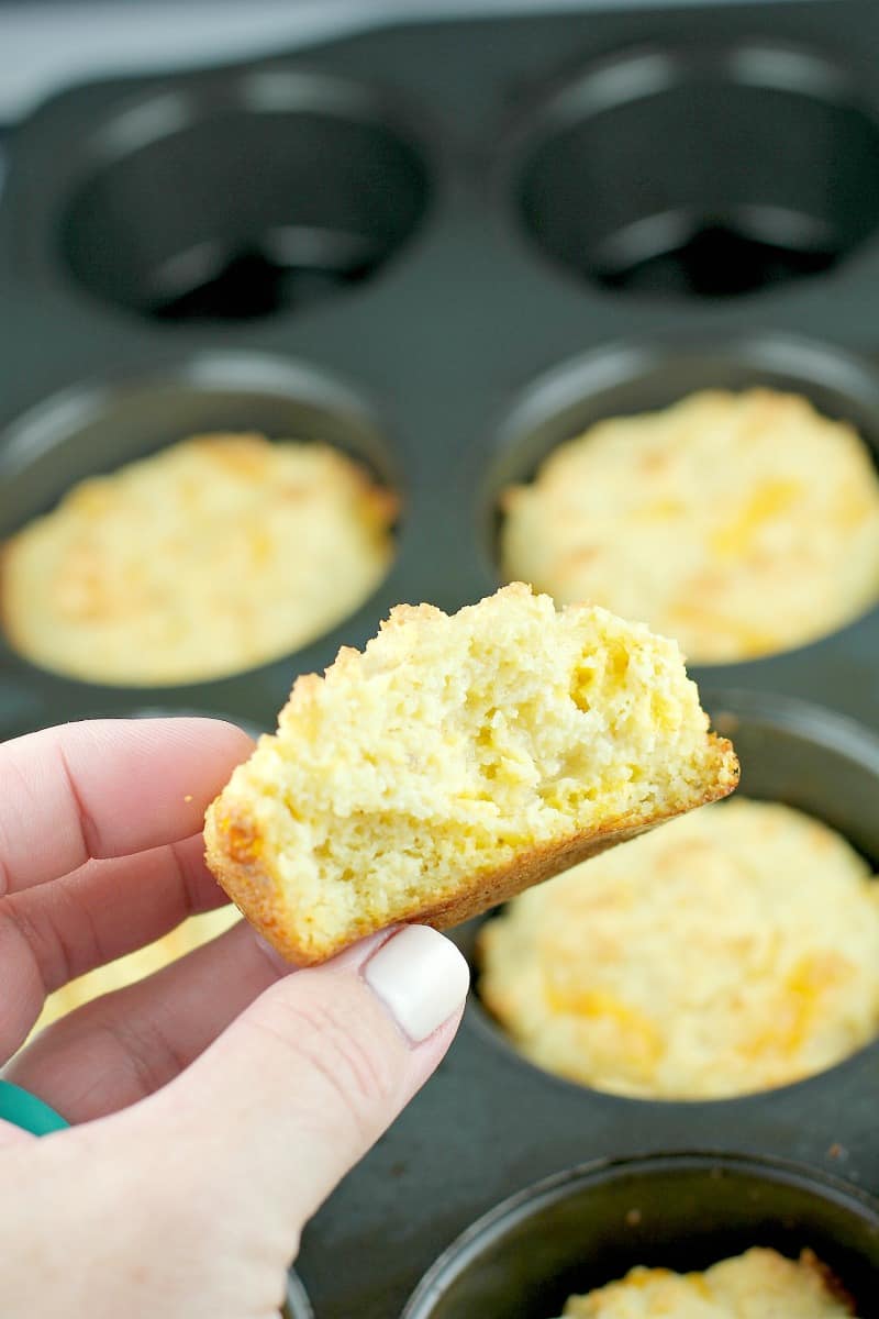 hand holding biscuit broken in half to show flaky inside, other biscuits in muffin tin in the background