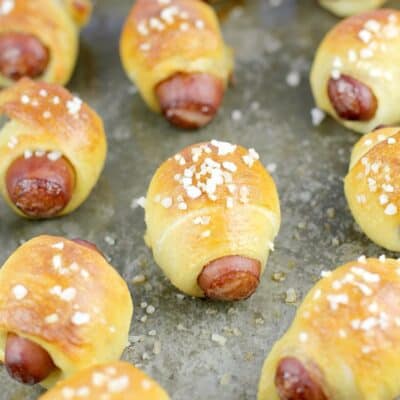 zoomed out view of cooked mini pigs in a blanket on a bake sheet sprinkled with salt