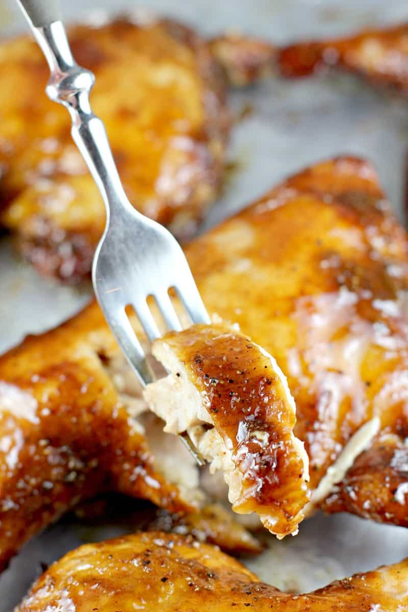 fork holding a bite of chicken; chicken quarters in the background
