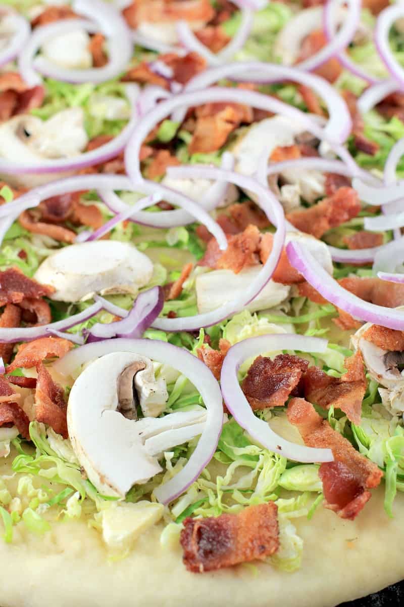 close view of mushrooms, onion, brussels sprouts and bacon on pizza dough