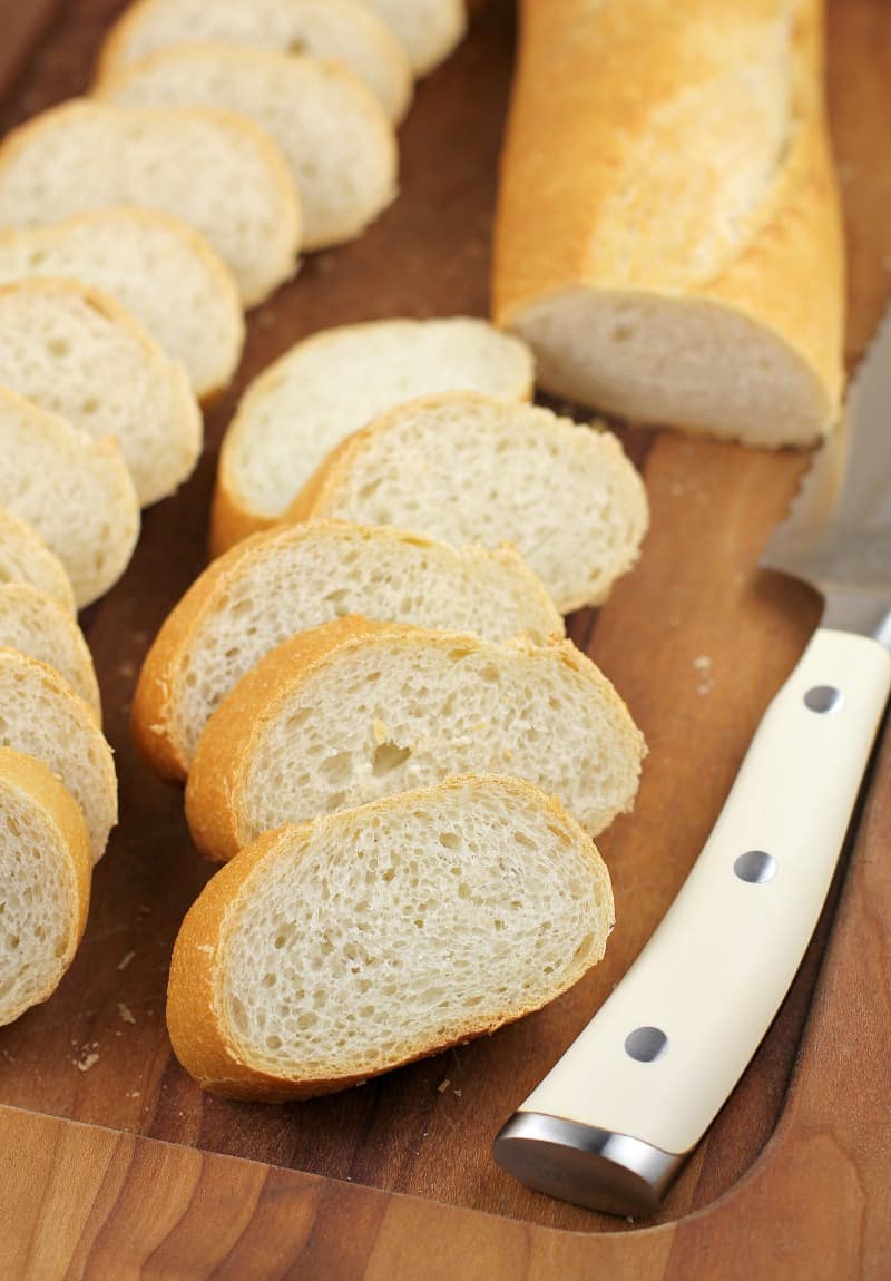 sliced baguette on wood board with bread knife