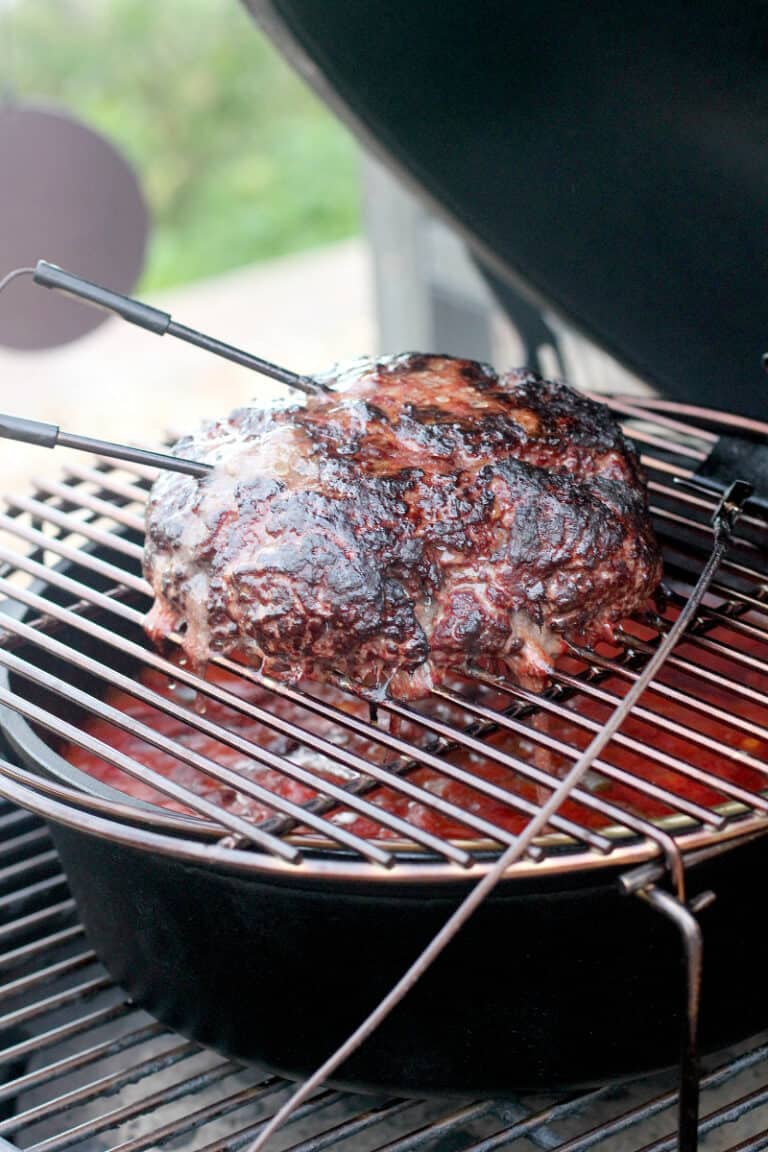 large loaf of smoked ground beef on grill grate in Big Green Egg with temperature probes sticking out