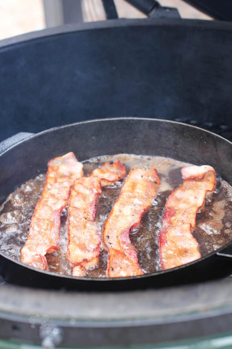 bacon cooking in cast iron skillet on grill
