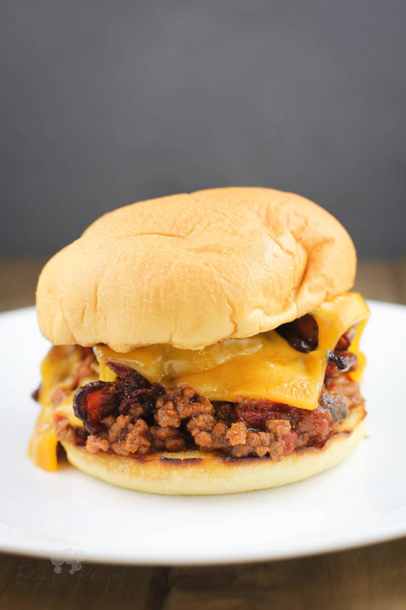 assembled recipe of grilled sloppy joe in a toasted bun with cheddar and bacon; on white plate