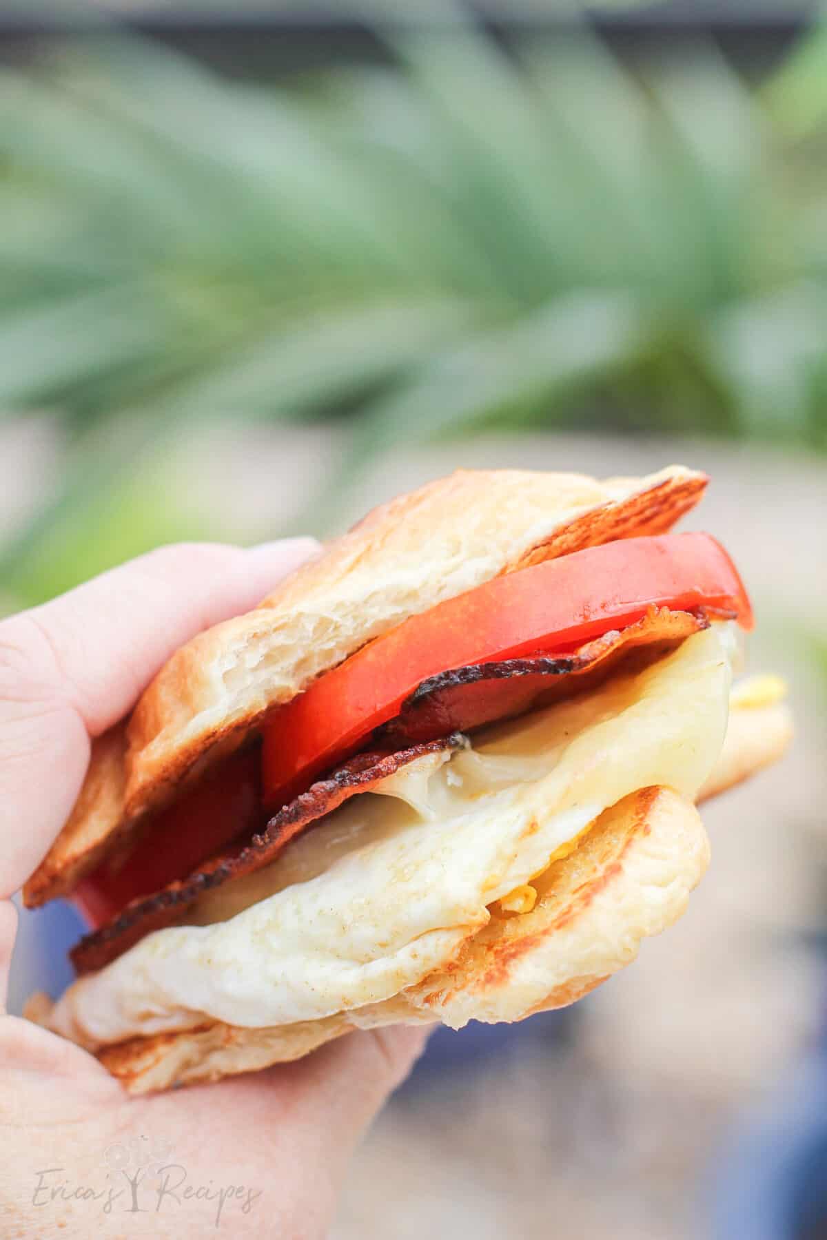 close side view of a hand holding a croissant breakfast sandwich