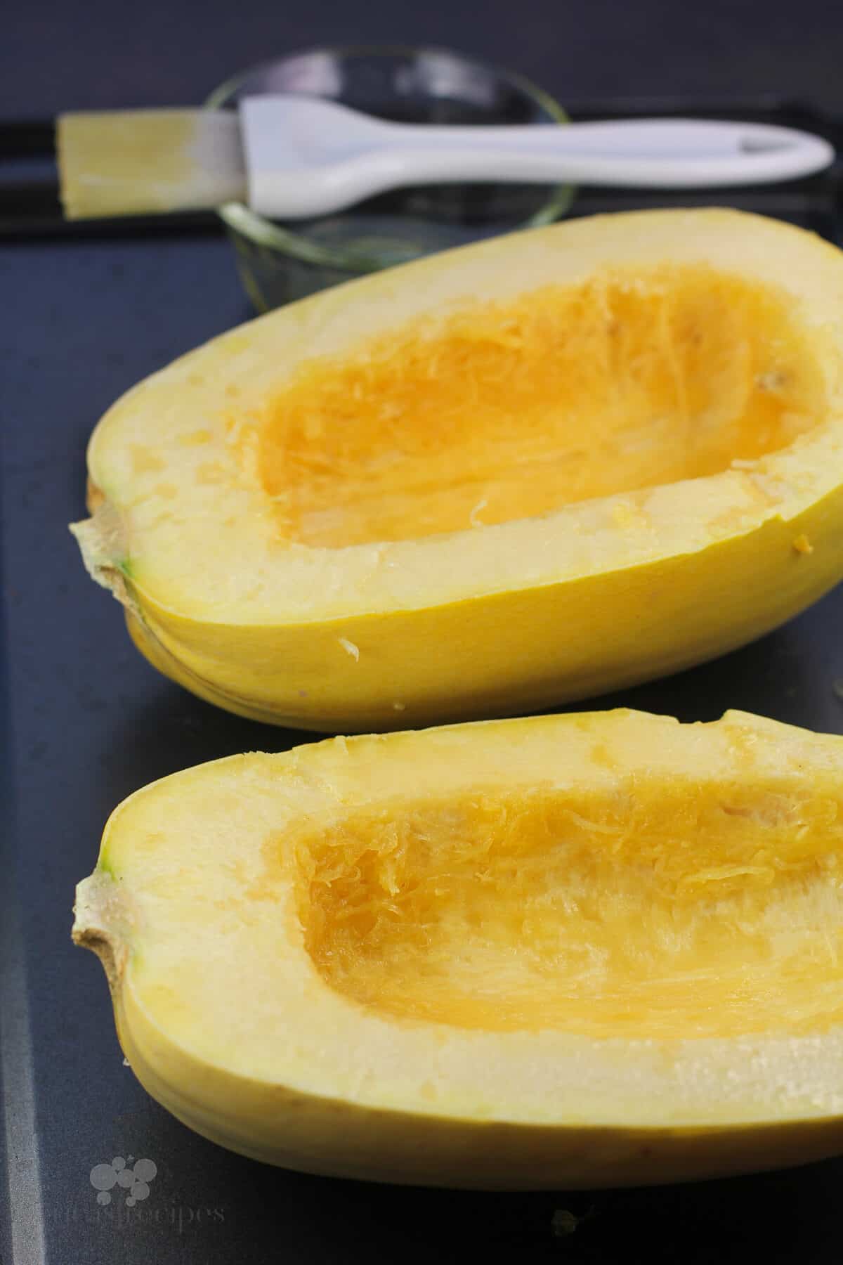 cut spaghetti squash halves on metal bake sheet