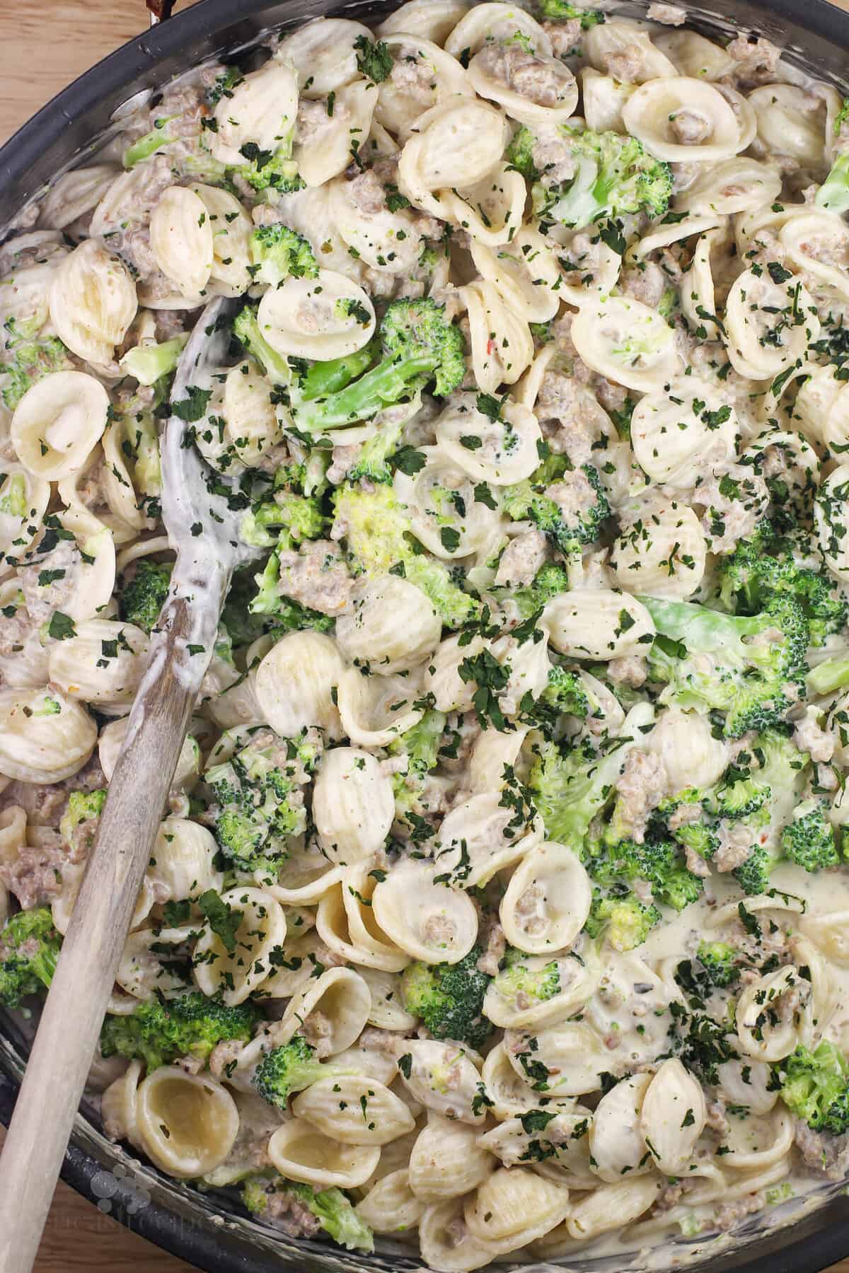 prepared pasta with sausage and broccoli in large pan with wood spoon