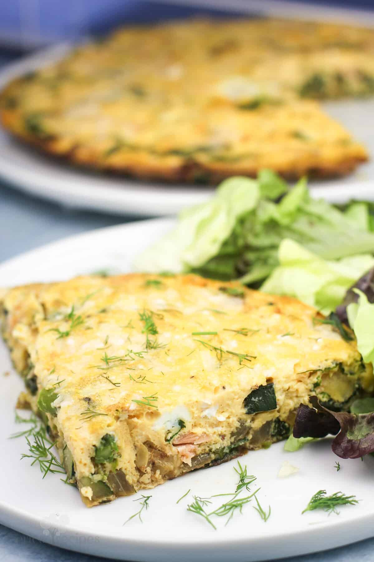 slice of vegetable frittata on white plate with salad