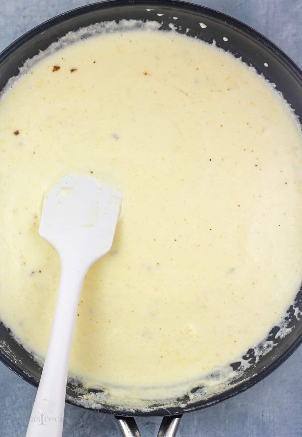 alfredo sauce in skillet with white rubber spatula