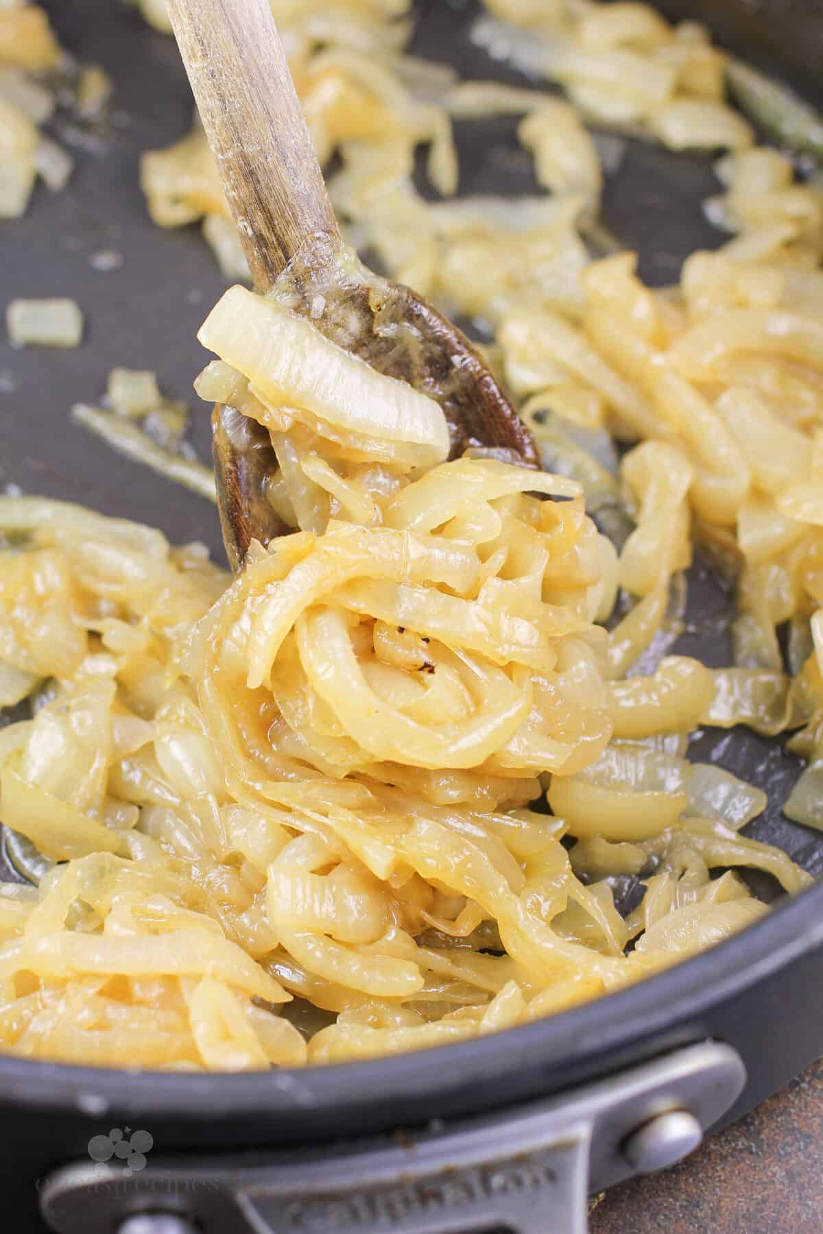 cooked onions in skillet with wood spoon