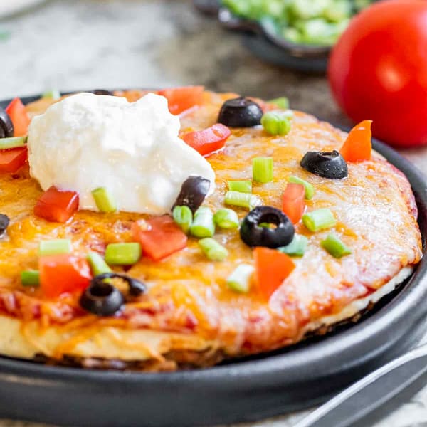Mexican pizza on a black plate on a white counter.