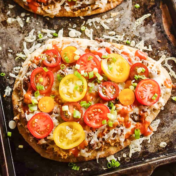 taco flatbread on bake sheet topped with sliced red and yellow tomatoes