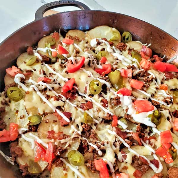 Irish nachos with taco meat, jalapenos, tomatoes, melted cheese and sour cream in a cast iron pan.