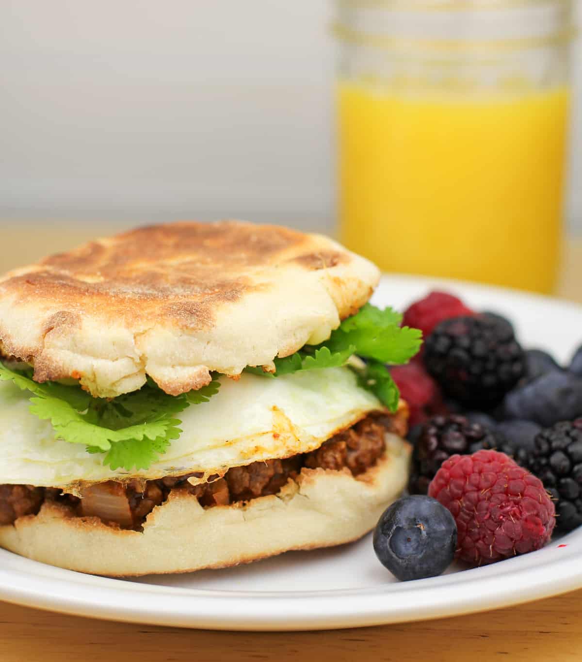 prepared breakfast sandwich on white plate next to berries