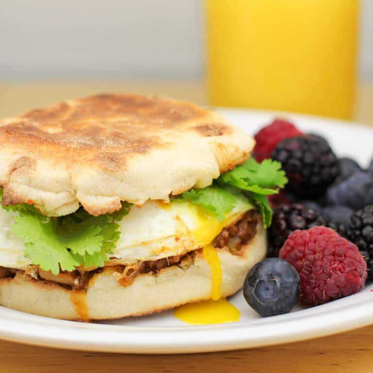 taco and egg sandwich on white plate next to berries. Yolk is visible down side of sandwich