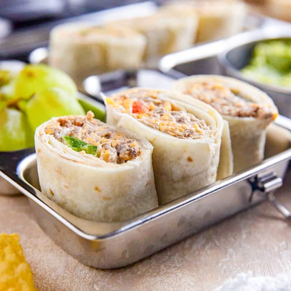 Taco meat pinwheels in a stainless steel meal prep container with guacamole and green grapes on the side.
