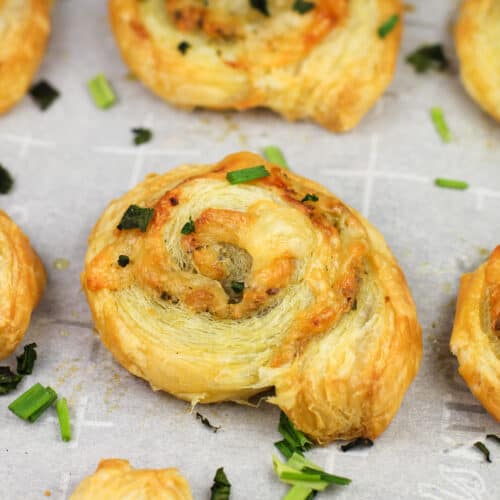 cooked pesto puffed pastry pinwheel on white parchment paper topped with chopped herbs