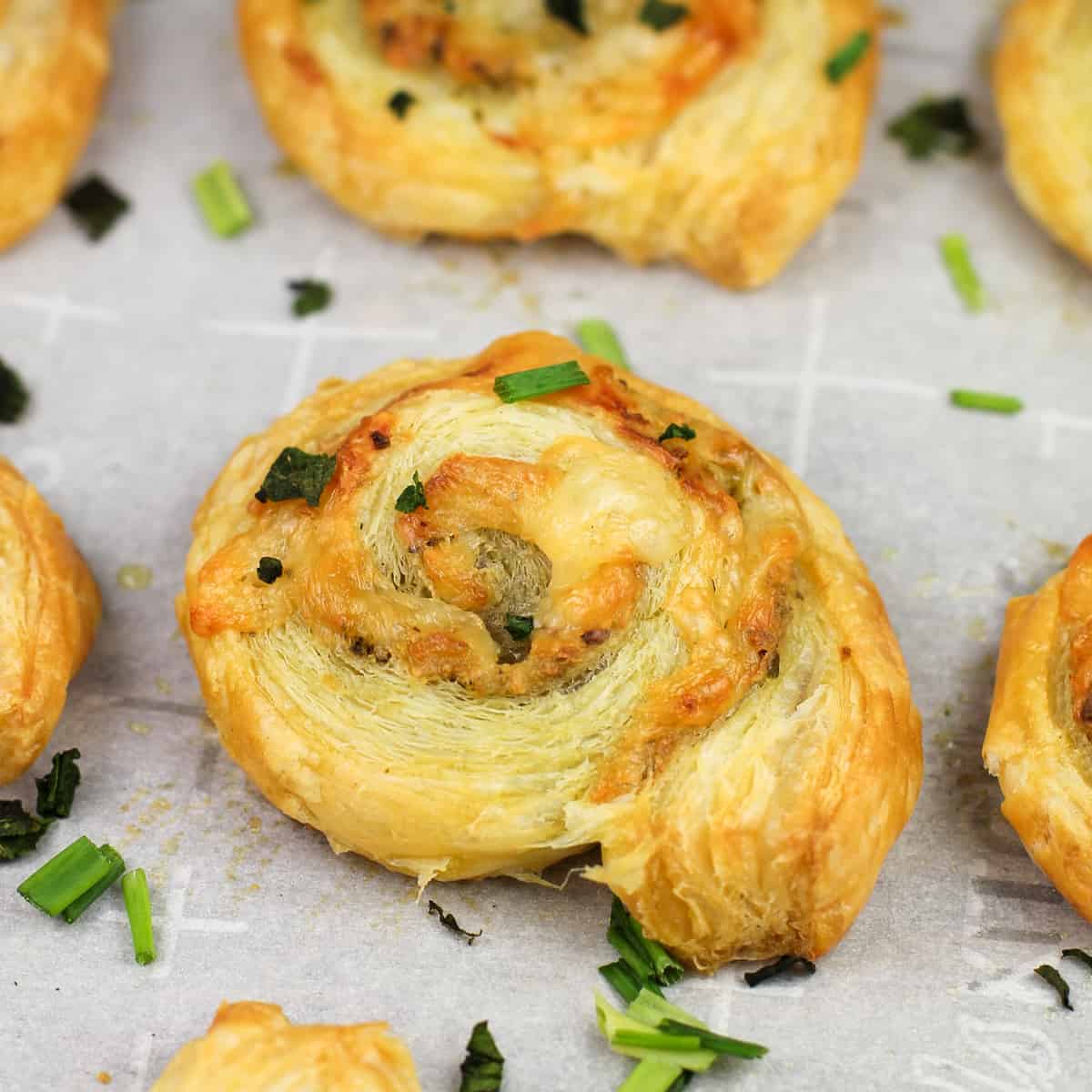 cooked pesto puffed pastry pinwheel on white parchment paper topped with chopped herbs