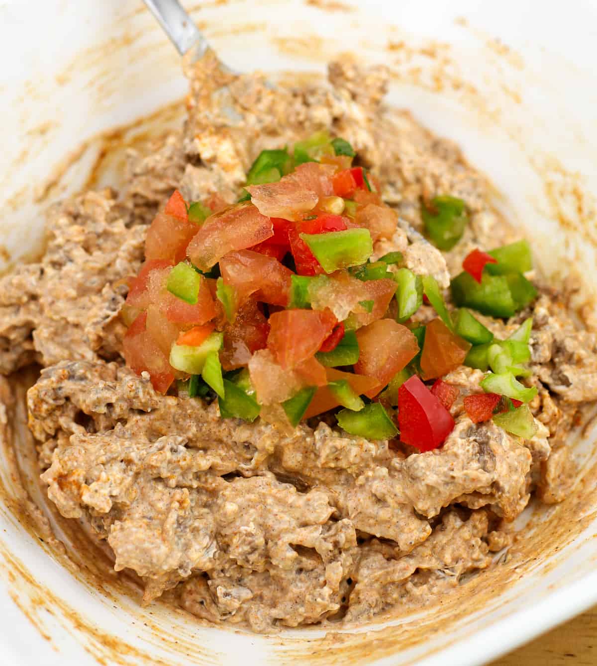 meat and cream cheese mixture in white bowl topped with chopped veggies
