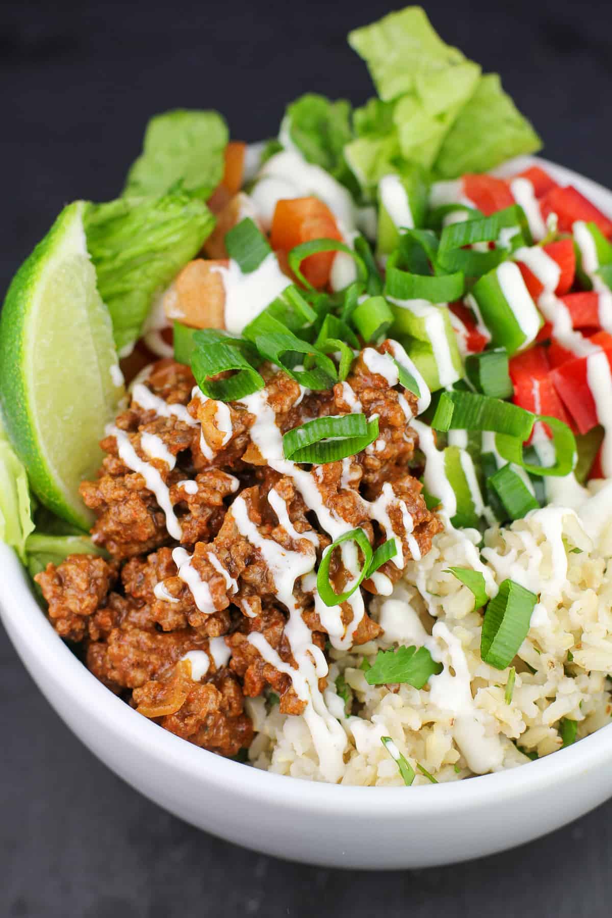 white bowl with taco meat, veggies, lettuce, brown rice, and a lime wedge