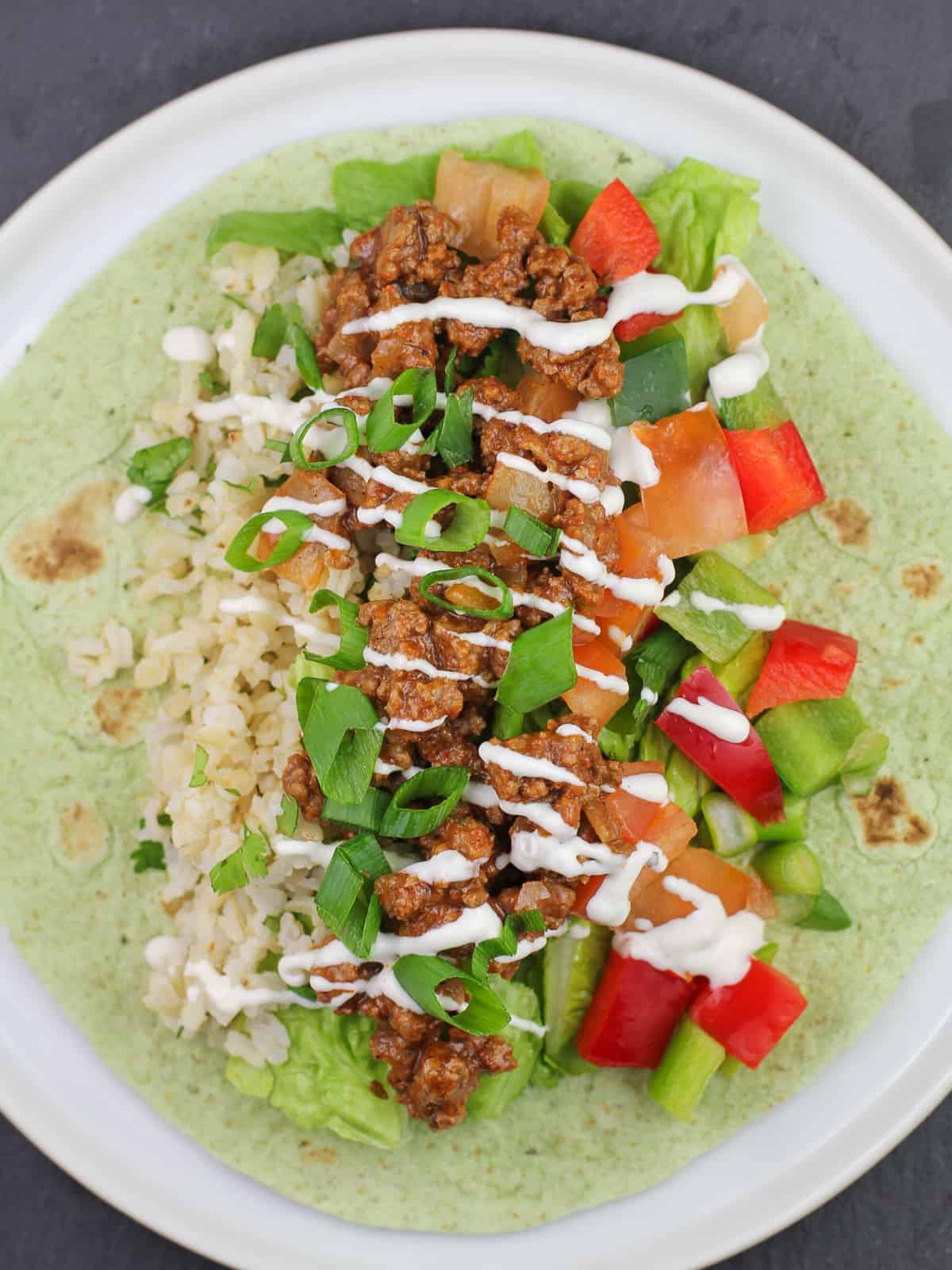 taco meat, veggies, and rice on top of spinach tortilla wrap topped with ranch dressing