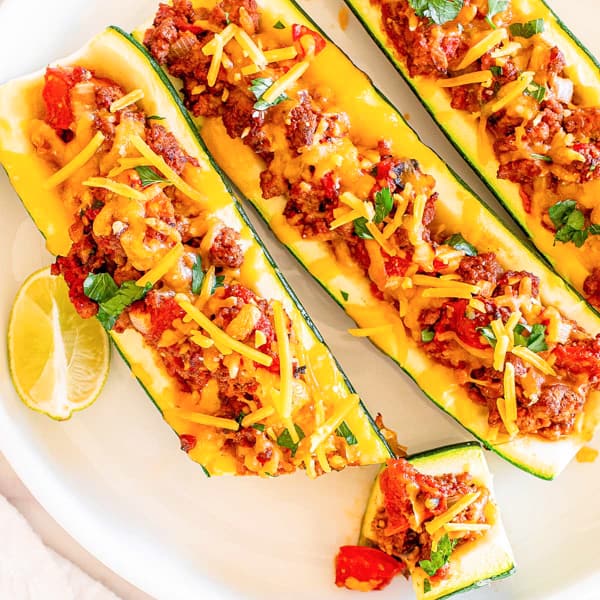 Taco stuffed zucchini boats with meat and cheese on a plate.